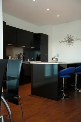 a kitchen with black cabinets and blue bar stools at The Spires Serviced Apartments Glasgow in Glasgow