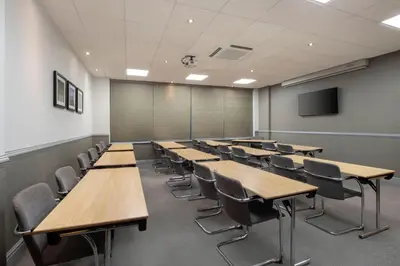 a classroom with wooden tables and chairs and a screen at Leonardo Royal Hotel Glasgow in Glasgow