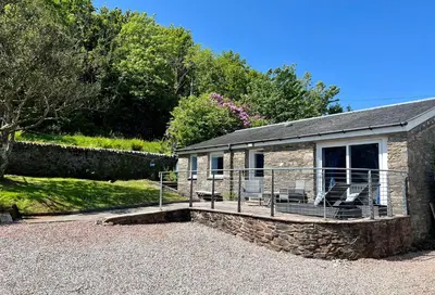a stone cottage with a deck and chairs on it at Craignethan in Kames