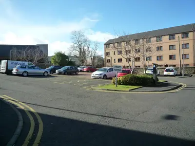 a parking lot with cars parked in front of a building at Paisley Central Apartment #3 in Paisley