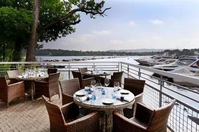 a patio with tables and chairs next to a boat at Cameron House on Loch Lomond in Balloch