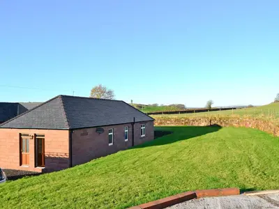a house on top of a grassy hill at Liftingstane Cottage in Closeburn