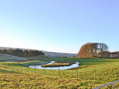 a river in a field with a fence at Liftingstane Cottage in Closeburn