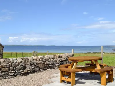 a wooden picnic table next to a stone wall at Charlies Cottage in Muasdale