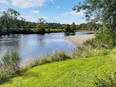 a river with a grassy field next to a body of water at Craig Lora in Dalmally