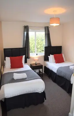 a bedroom with two beds with red pillows and a window at Kelpies Serviced Apartments Alexander- 2 Bedrooms in Falkirk