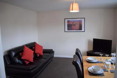 a living room with a black leather couch and a table at Kelpies Serviced Apartments Alexander- 2 Bedrooms in Falkirk