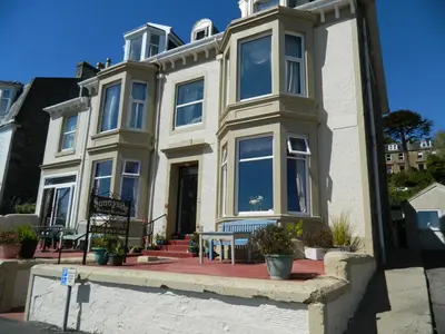 a white house with a bench in front of it at Sunnyside House in Rothesay