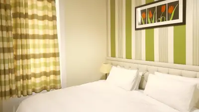 a bedroom with a white bed with green and yellow stripes at Loch Lomond Apartments in Dumbarton