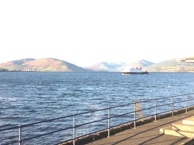 a boat on a large body of water with mountains at Commodore Guesthouse, Seaside Holiday Suites in Rothesay