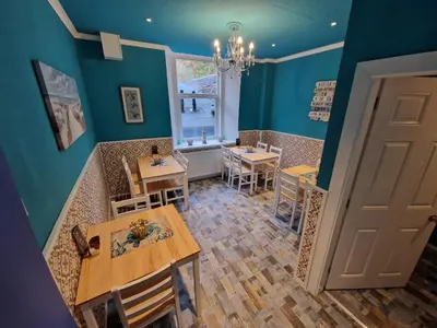a dining room with blue walls and tables and a window at Commodore Guesthouse, Seaside Holiday Suites in Rothesay