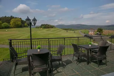 a patio with tables and chairs and a golf course at Glasgow Westerwood Hotel, Spa & Golf Resort in Cumbernauld