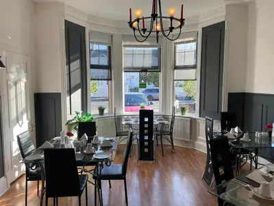 a dining room with tables and chairs and windows at Beechwood Ensuite Guest House in Ayr