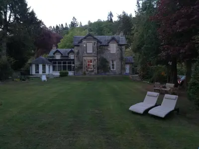 a house with two white chairs in a yard at Lubnaig Guest House in Callander