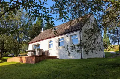 a small white house on a green lawn at Larch Cottage in Blairmore