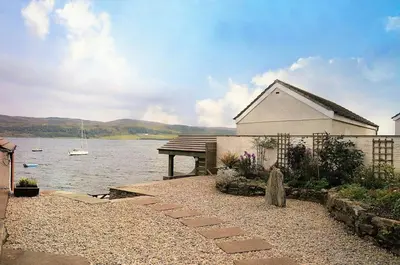 a building next to a body of water with a boat at Taigh na Mara in Kames