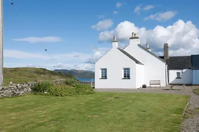 a white house with a green lawn in front of it at Aird Farm Holiday Cottages in Ardfern
