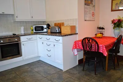 a kitchen with white cabinets and a table with a red table cloth at Culzean House in Ardentinny