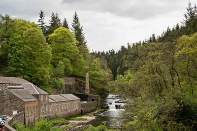 a river flowing through a forest next to a building at New Lanark Mill Hotel in Lanark