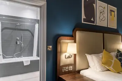 a bedroom with a bathroom with a shower and a bed at voco Grand Central Glasgow by IHG in Glasgow
