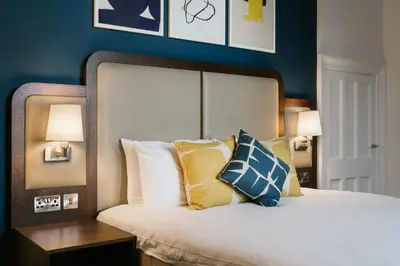 a bedroom with a bed with blue walls and pillows at voco Grand Central Glasgow by IHG in Glasgow