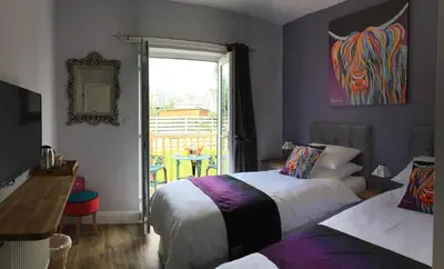 a bedroom with two beds and a table and a window at Angel Cottage in Drymen