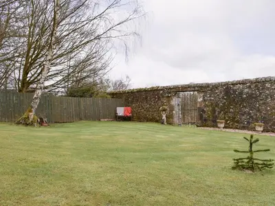 a yard with a stone wall and a fence at Kinneddar Cottage in Saline