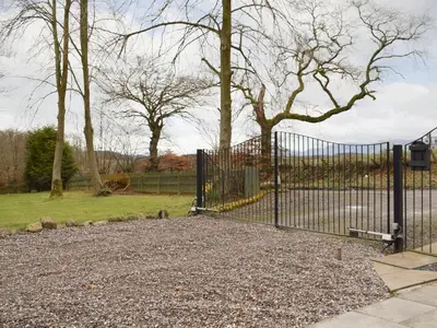 a black gate in a park with trees and grass at Kinneddar Cottage in Saline