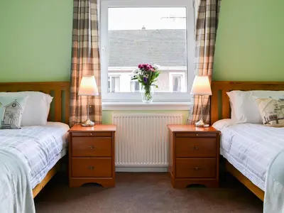 a bedroom with two beds and a window with a vase of flowers at Harbour View in Oban