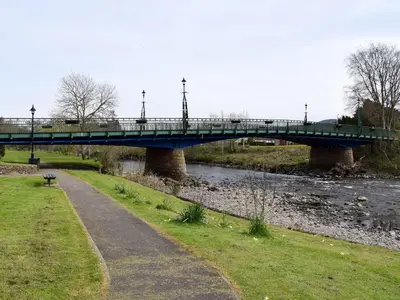 a blue bridge over a river with a path at Caroch Cottage in Comrie