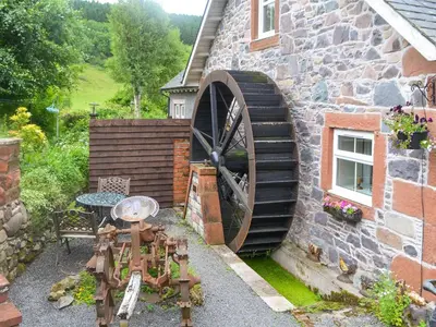 a stone building with a large wheel next to a building at The Cottage in Blackwood