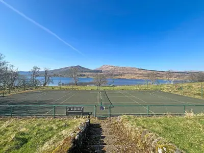 a tennis court with a bench next to a tennis court at Bonnie's Bothy in Port of Menteith