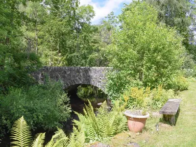 an old stone bridge with a bench in a park at Bonnie's Bothy in Port of Menteith