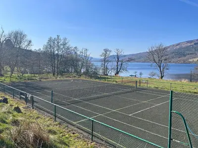 a tennis court next to a body of water at Grace's Cottage in Port of Menteith