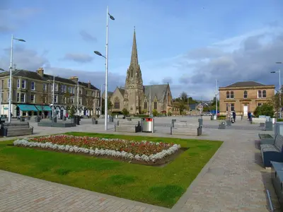 a town square with a park with flowers and a church at Snug - Krayr Apartment in Helensburgh