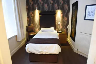a bedroom with a bed with a headboard and a chair at Sandyford Hotel in Glasgow