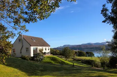 a house on a hill with a lake in the background at Rowan Cottage in Blairmore