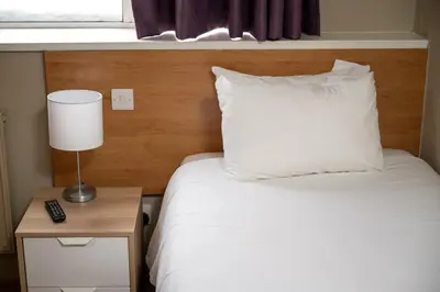a bed with a white pillow and a lamp on a night stand at The Titan By Greene King Inns in Clydebank