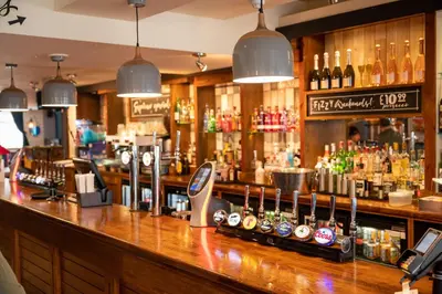 a bar with a counter with a lot of drinks at The Titan By Greene King Inns in Clydebank