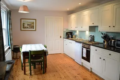 a kitchen with white cabinets and a table in it at Teal Cottage in Clachan of Glendaruel