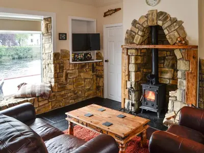 a living room with a stone wall and a wood stove at Minnow Cottage in Newton Stewart