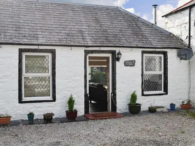 a white house with a door and some plants at Minnow Cottage in Newton Stewart