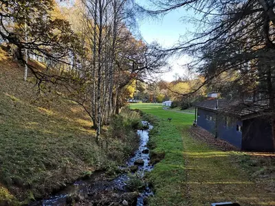 a creek in a field with trees and a house at Loch Monzievaird Chalets in Crieff