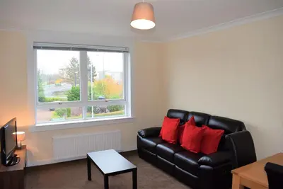 a living room with a black leather couch and a window at Kelpies Serviced Apartments MacGregor- 2 Bedrooms in Grangemouth