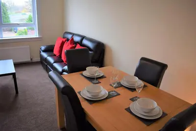 a dining room with a table and a couch at Kelpies Serviced Apartments MacGregor- 2 Bedrooms in Grangemouth