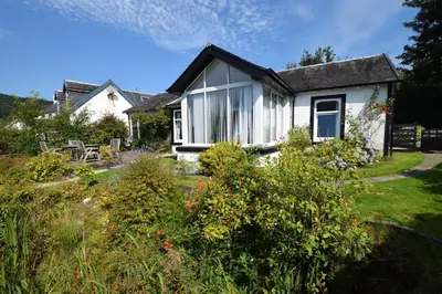 a small white house with a garden in front of it at Ashburn Cottage in Lochgoilhead