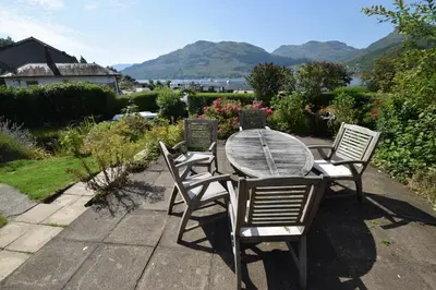 a wooden table and chairs with mountains in the background at Ashburn Cottage in Lochgoilhead
