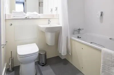 a white bathroom with a sink and a toilet and a tub at The Raven’s Cliff Lodge by Marston's Inns in Motherwell
