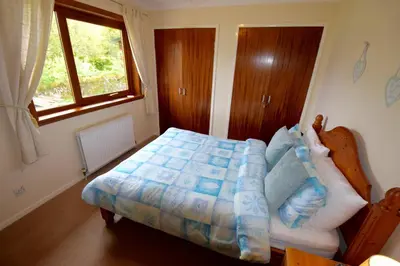 a bedroom with a bed with a blue comforter and a window at Cobbler View No. 1 in Lochgoilhead