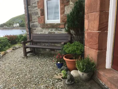 a wooden bench sitting next to a building with plants at Dunivaig B&B in Tarbert